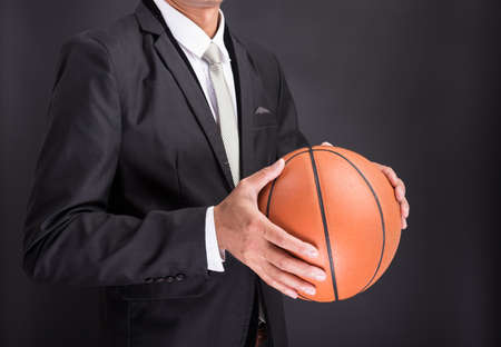 Young businessman holding basketball ball isolated on black backgroundの写真素材