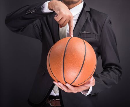 Young businessman holding basketball ball isolated on black backgroundの写真素材