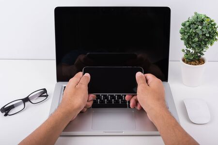 Young man working using mobile phone and laptop on white deskの写真素材