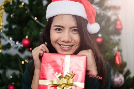 Smiling Young woman in santa helper hat with gift red box at front Christmas tree, Christmas or New Year conceptの写真素材