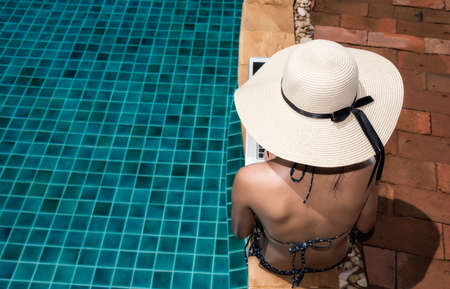 Asian Young woman in big hat relaxing on poolside with laptop computer blue waterの写真素材