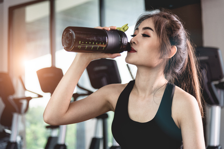 Sports young woman with protein cocktail in shaker sitting in fitness gym. Sports nutrition.の写真素材