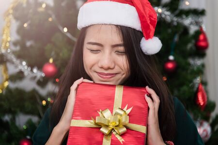 Smiling Young woman in santa helper hat with gift red box at front Christmas tree, Christmas or New Year conceptの写真素材