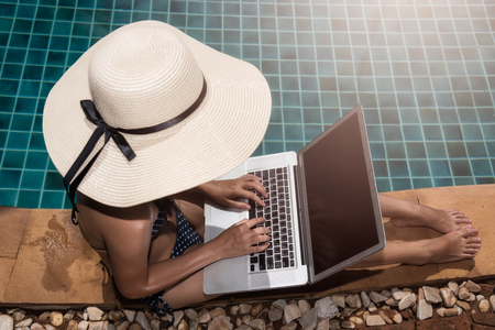Asian Woman working on laptop computer sitting at poolside blue waterの写真素材
