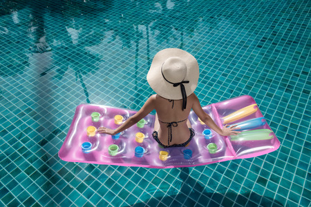 Portrait beautifu woman relaxing in big hat and bikini Sitting back on air mattress in swimming pool blue waterの写真素材