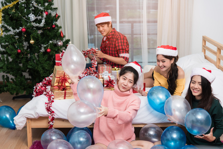 Group of friends celebrating Christmas at home throwing balloon up, Christmas or New Year conceptの写真素材