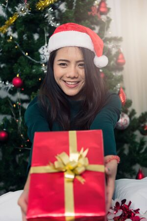 Smiling Young woman in santa helper hat with gift red box at front Christmas tree, Christmas or New Year conceptの写真素材