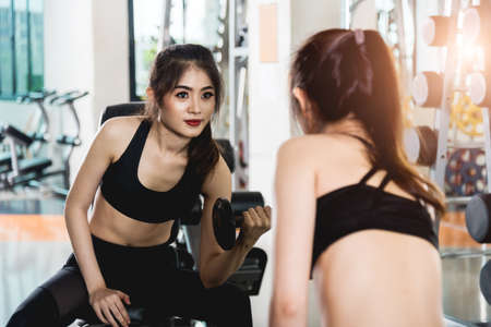 Attractive young woman Glass mirror working out with dumbbells at gymの写真素材