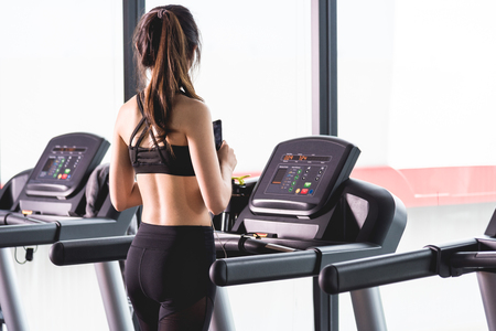 Back Attractive sports woman on running track listening music with mobile phone in hand using earphonesの写真素材