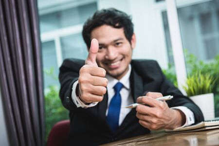Business man smiling showing thumbs up, focus handの写真素材