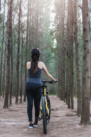 Back young female woman helmet catch bicycle at forest on summer with copy spaceの写真素材