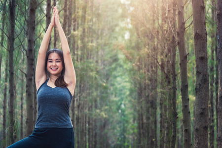 Beautiful happy young female woman relaxation standing outdoor fitness exercise yoga in forest tree nature park with copy spaceの写真素材