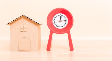 Cardboard paper model house and red clock, investment plan concept