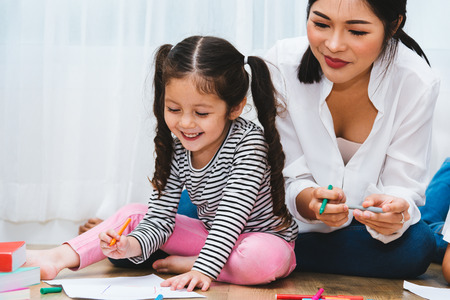 Happy child kid girl son kindergarten drawing on peper teacher education with beautiful mother at...