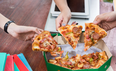 Hands taking pizza slices from green boxの写真素材