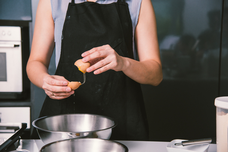Woman girl baker in kitchen cooking whisk egg to bowlの写真素材