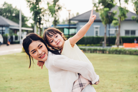 Family happy children kid son girl kindergarten playing ride back piggyback mother mom on outdoors parkの写真素材