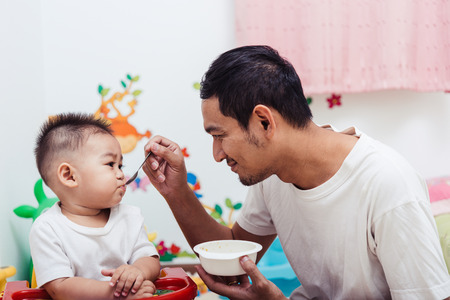 Family father dad eating feeding food baby boy son on chair at homeの写真素材