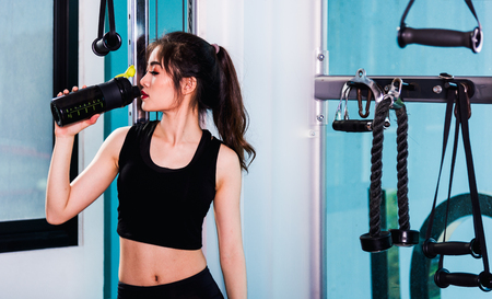 Young woman drinking water on bottle after workout at fitness gymの写真素材