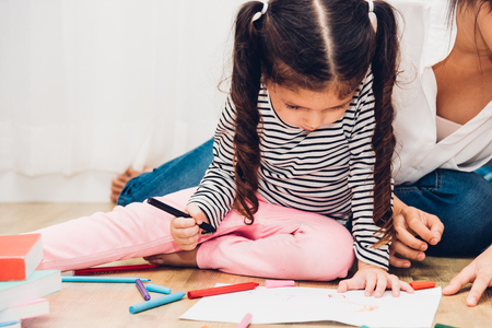 Happy child kid girl son kindergarten drawing on peper teacher education with beautiful mother at interior room homeの写真素材