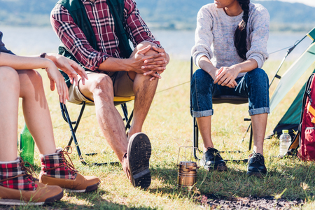Young couple and friend sitting on chair discuss together on camping tent in summer, focus legの写真素材