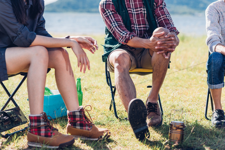 Young couple and friend sitting on chair discuss together on camping tent in summer, focus legの写真素材
