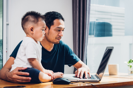 Man father working on laptop computer with son from homeの写真素材