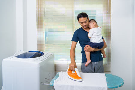 Man father ironing clothes son and he carry son in homeの写真素材