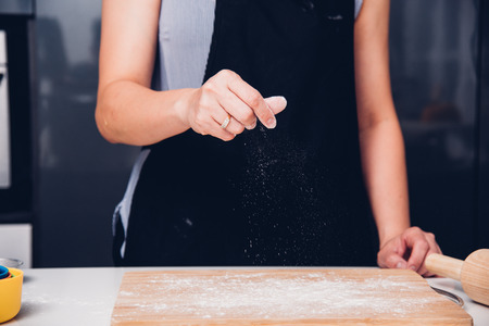 Hands of baker woman female making sprinkling flour dough on table