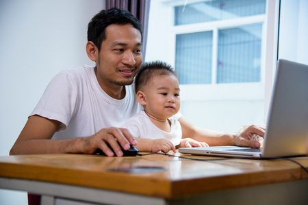 Man father using working on laptop computer with son in homeの写真素材