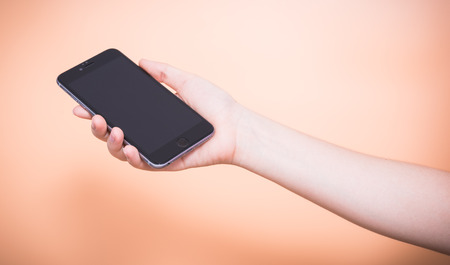 Female holding mobile smartphone plus blank screen on orange color backgroundの写真素材