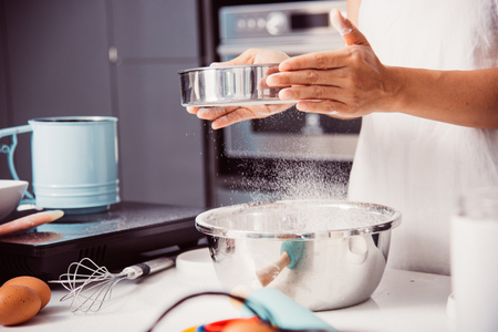 Woman girl in kitchen cooking baker bakery powder dough with baker sieve siftingの写真素材