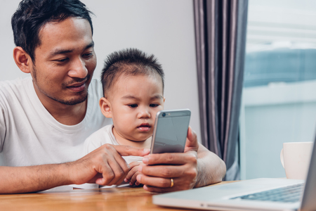 Man father working on laptop computer and using smartphone technology with son from homeの写真素材