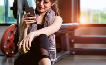 Young woman girl sitting lifestyle using smartphone after training exercise workout at fitness gymの写真素材