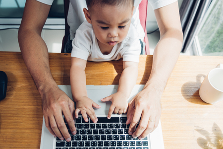 Man father using working on laptop computer with son in homeの写真素材