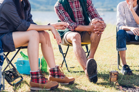 Young couple and friend sitting on chair discuss together on camping tent in summer, focus legの写真素材