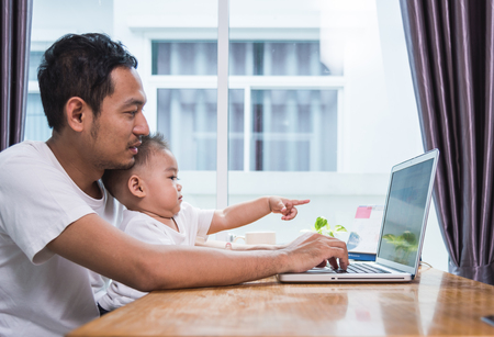Man father using working on laptop computer with son in homeの写真素材