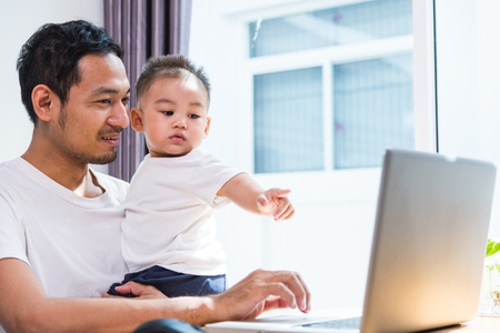 Man father using working on laptop computer with son in homeの写真素材