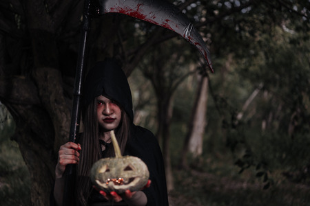 Woman ghost horror her have scythe and pumpkin on hand in forest, halloween day conceptの写真素材