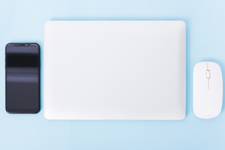 Top view close cover laptop computer notebook, smart phone and wireless mouse isolated on blue backgroundの写真素材