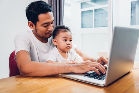 Man father using working on laptop computer with son in homeの写真素材