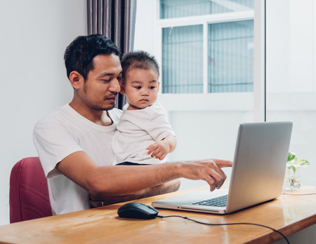Man father using working on laptop computer with son in homeの写真素材