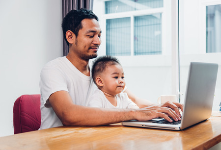 Man father using working on laptop computer with son in homeの写真素材