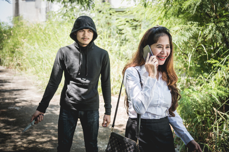 The robber holding a knife Is going to rob on back her while women are talking on mobile phoneの写真素材
