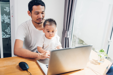 Man father using working on laptop computer with son in homeの写真素材
