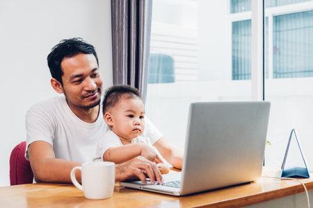 Man father using working on laptop computer with son in homeの写真素材