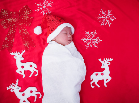 Newborn baby sleeping on santa het and red background, christmas or happy new year conceptの写真素材