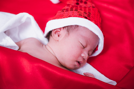 Newborn baby sleeping on santa het and red background, christmas or happy new year conceptの写真素材