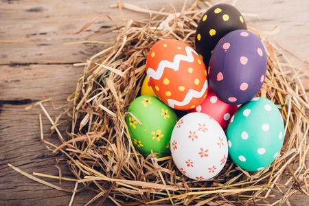 Beautiful Easter multi color egg in straw on wooden background, Easter day conceptの写真素材