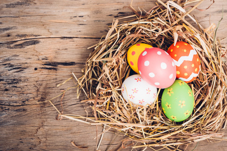 Beautiful Easter multi color egg in straw on wooden background, Easter day conceptの写真素材